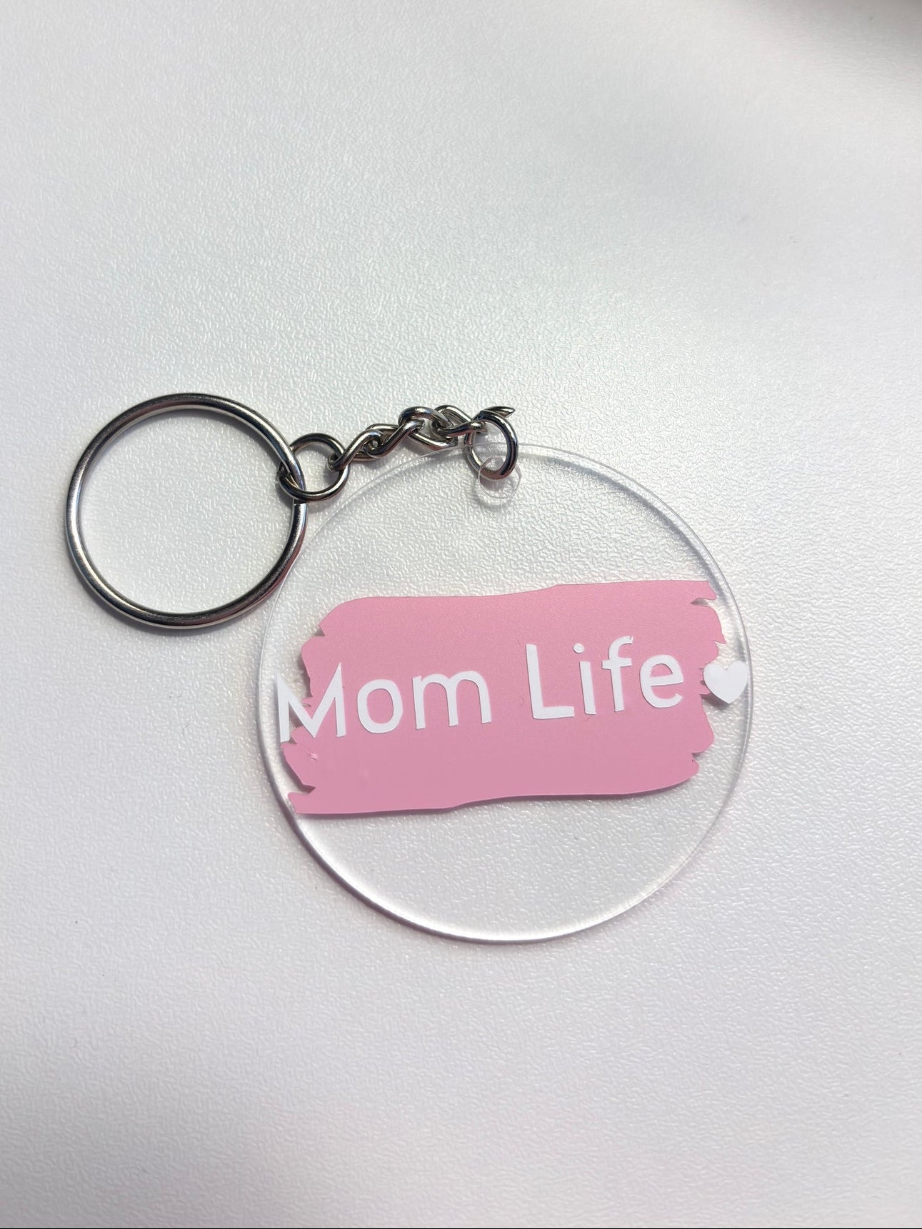 Clear acrylic keychain with pink label reading 'Mom Life' on a white background offered at Pennie's Little Keepsakes . Michigan Made