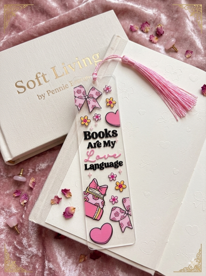 Decorative bookmark with pink tassel on a book titled 'Soft Living by Pennie' on a pink textured surface.